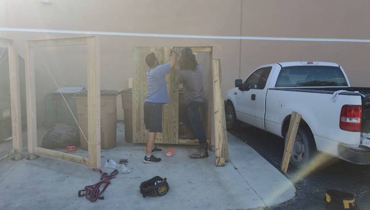 Two crew members building a wood dumpster enclosure gate beside a pickup truck