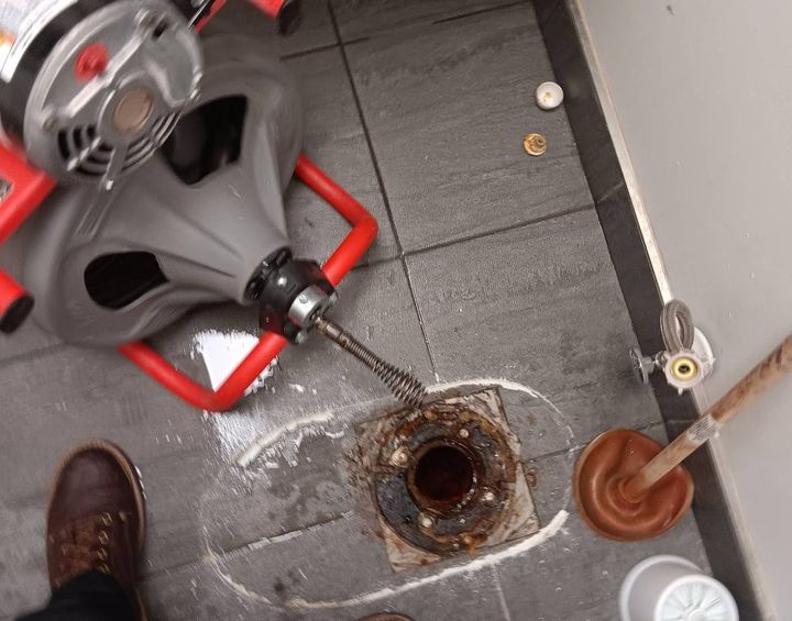 Drain machine cable clearing an open floor drain in a commercial restroom