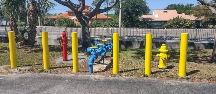 Freshly painted yellow safety bollards, red and yellow fire hydrants, and blue pump assembly at a commercial property