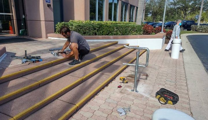 Crew member installing a metal handrail on commercial stairs with yellow anti-slip nosing